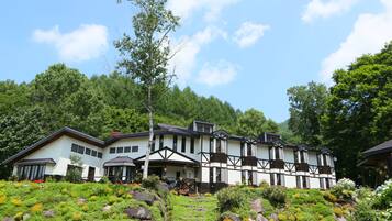 A large, multi-story building with a traditional architectural style, surrounded by lush greenery and a clear sky.