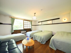 Una habitación con dos camas individuales, un sofá, una pequeña mesa redonda con un florero y una ventana con cortinas.