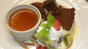 Ein Dessertteller mit kleiner Soßen-Schale, Kuchenstück, Schlagsahne, Kiwi und Erdbeere.