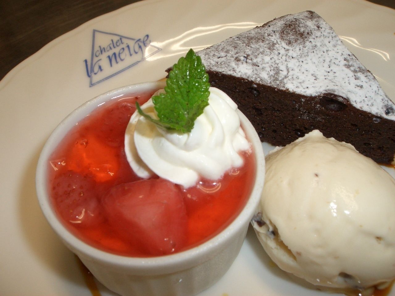 A dessert plate with a slice of cake and a bowl of fruit compote with whipped cream and a mint leaf.