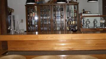 A wooden bar area with a glass cabinet displaying bottles and glasses, two black lamps, and three woven placemats on the floor.