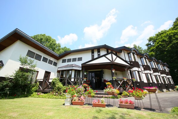 A large, two-story building with a prominent entrance, surrounded by lush gardens and potted plants. - Chalet La Neige (Minakami)