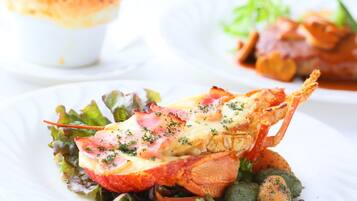 A lobster tail with melted cheese and herbs on a bed of greens, served on a white plate.