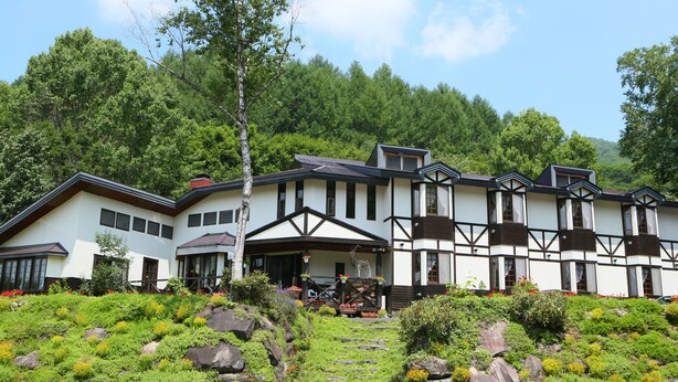 A large, multi-story building with a traditional architectural style, surrounded by lush greenery and a stone pathway leading to the entrance. - Chalet La Neige (Minakami)