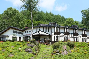 Un edificio grande de varios pisos con un estilo arquitectónico tradicional, rodeado de abundante vegetación y un camino de piedra que lleva a la entrada.