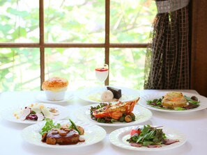 Una mesa con diversos platos, incluyendo mariscos y ensaladas, frente a una ventana con vistas a la vegetación.