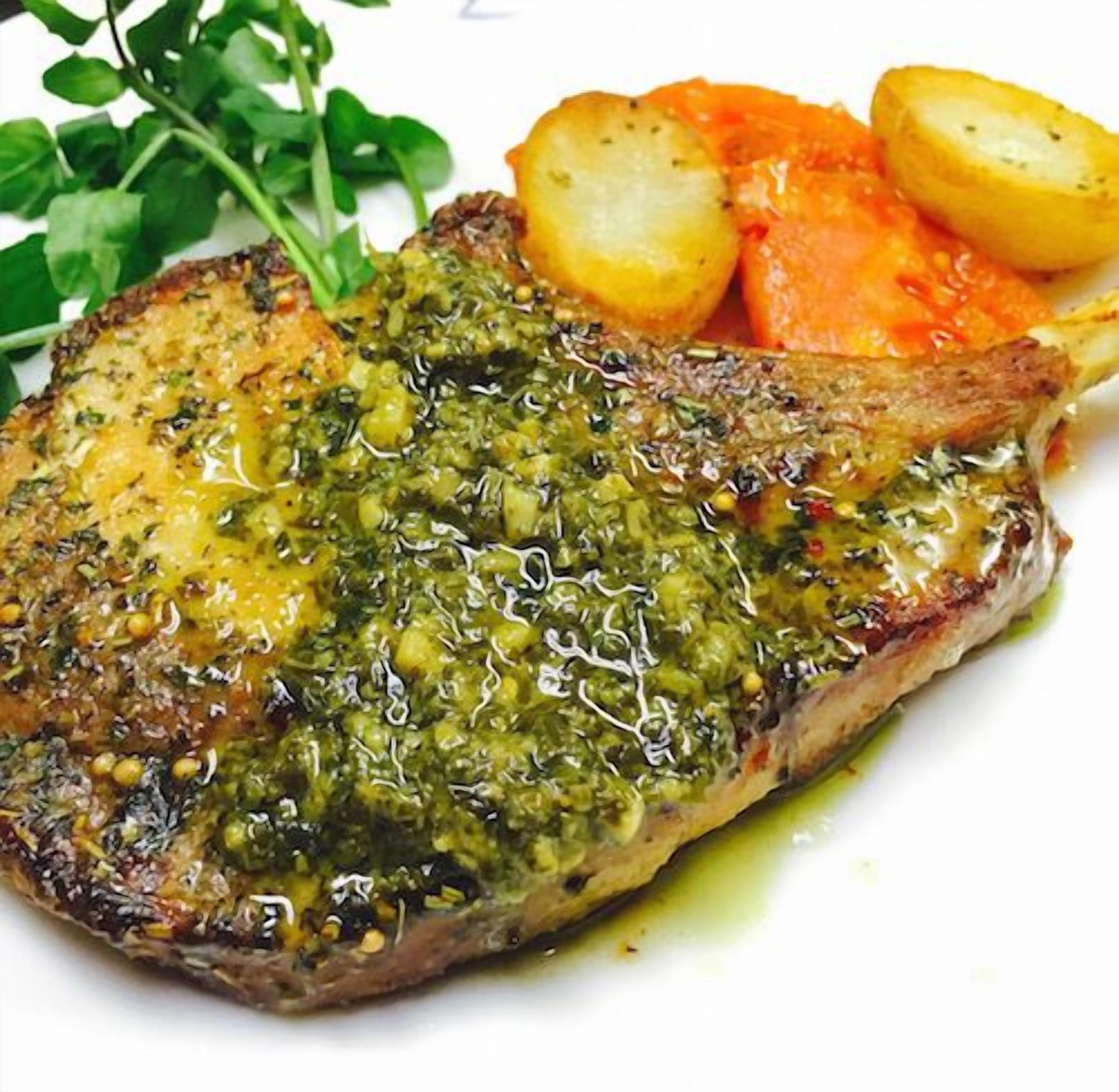 A steak with a green herb sauce, accompanied by roasted potatoes and a side of carrots.
