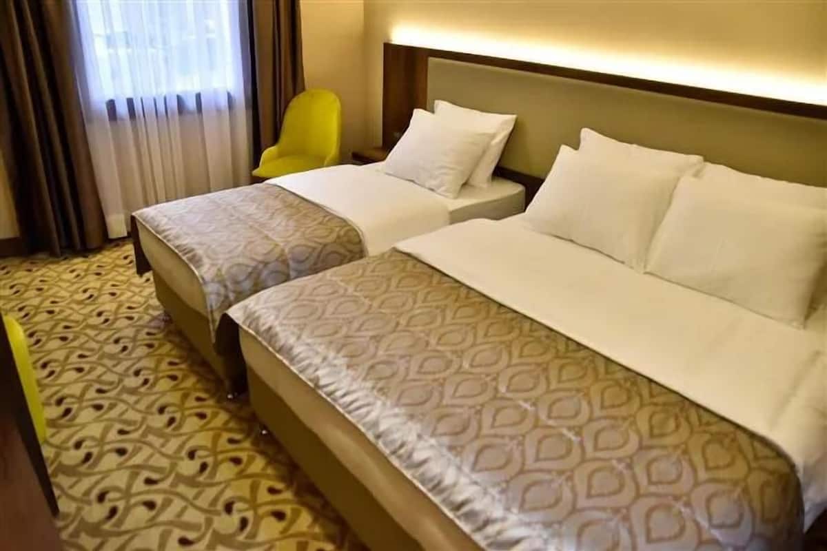 Une chambre d’hôtel avec deux lits, une moquette à motifs, une chaise jaune et une fenêtre avec des rideaux.