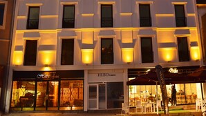 Ein mehrstöckiges Hotel mit einer symmetrischen Fassade, gleichmäßig verteilten Fenstern und einem Restaurant im Erdgeschoss mit Außenbereich.