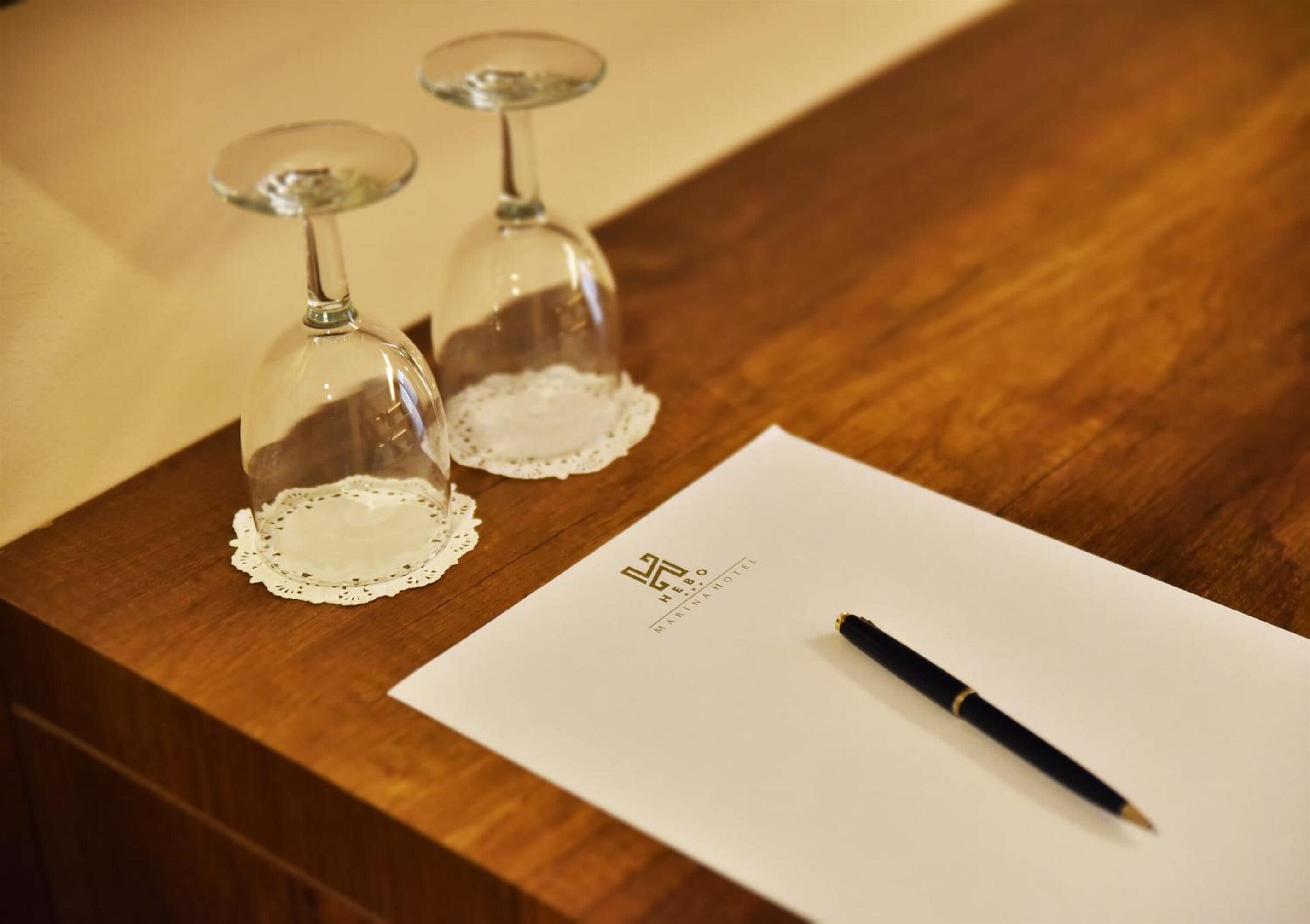 Two wine glasses on a wooden table with a pen and a piece of paper.