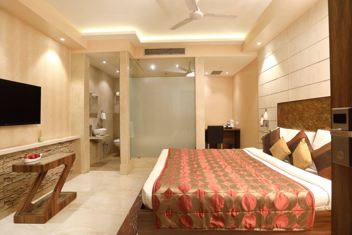 A modern hotel room with a large bed, a flat-screen TV, a desk, and a shower area.