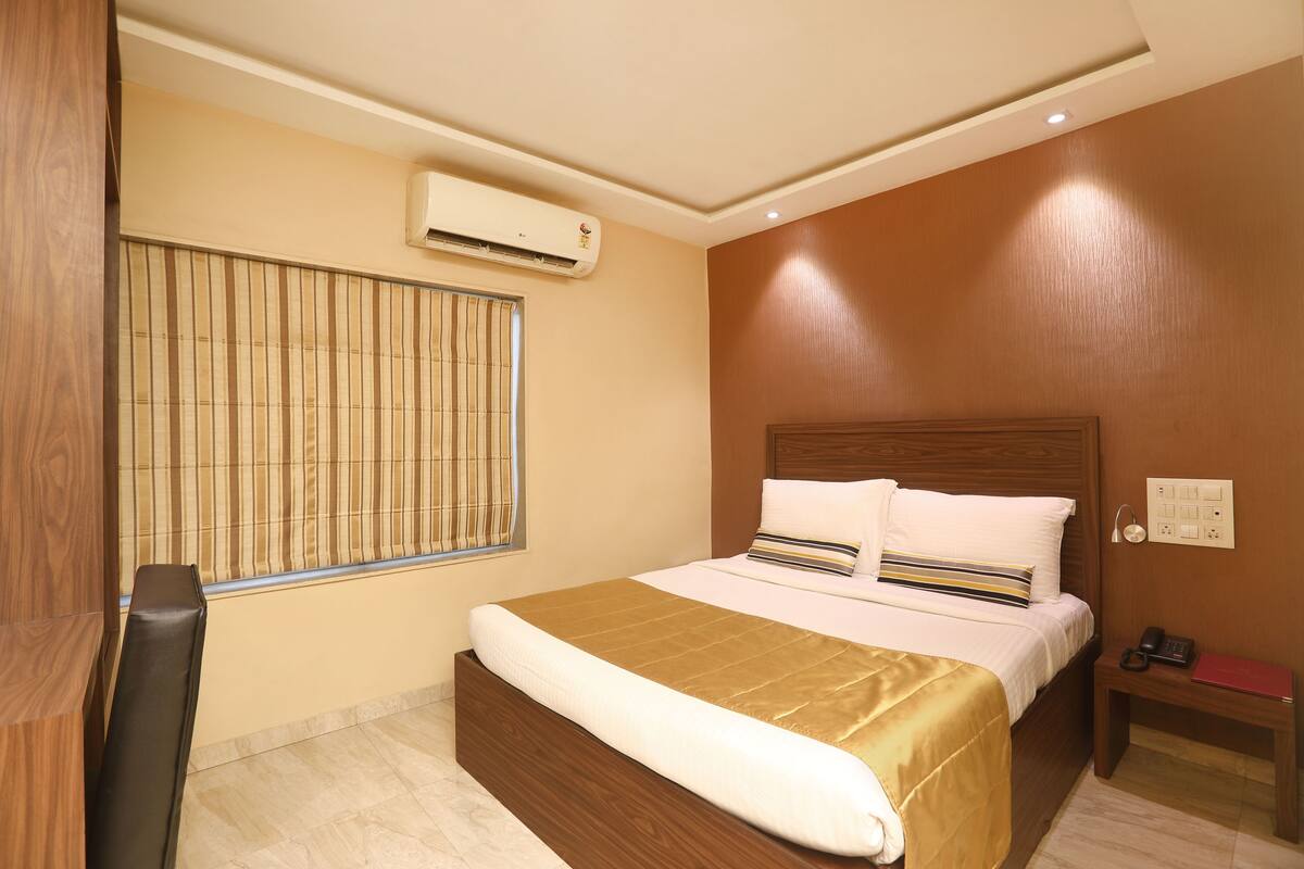 A hotel room with a bed, bedside table, and an air conditioning unit.