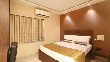 A hotel room with a bed, bedside table, and an air conditioning unit.