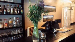 Una zona de bar con una variedad de botellas de licor, un jarrón con flores, un altavoz y un cuadro en la pared.