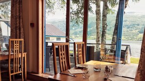 Un comedor con una mesa y sillas de madera, vista a un lago y un edificio al otro lado del agua.