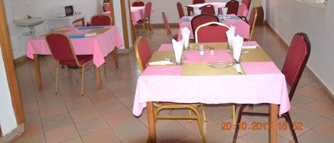 Un comedor con varias mesas dispuestas para comer, cada una con mantel rosa y sillas rojas.
