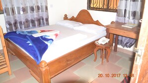 A bedroom with a wooden bed, a bedside table with a phone, and curtains with a floral pattern. - Motel 88 (Morogoro)