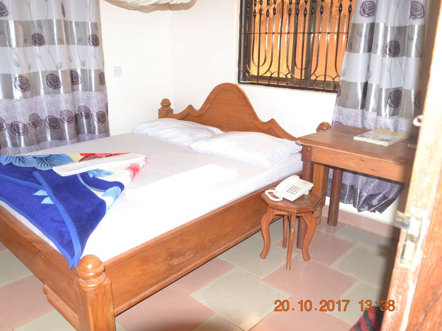 A bedroom with a wooden bed, a bedside table with a phone, and curtains with a floral pattern.