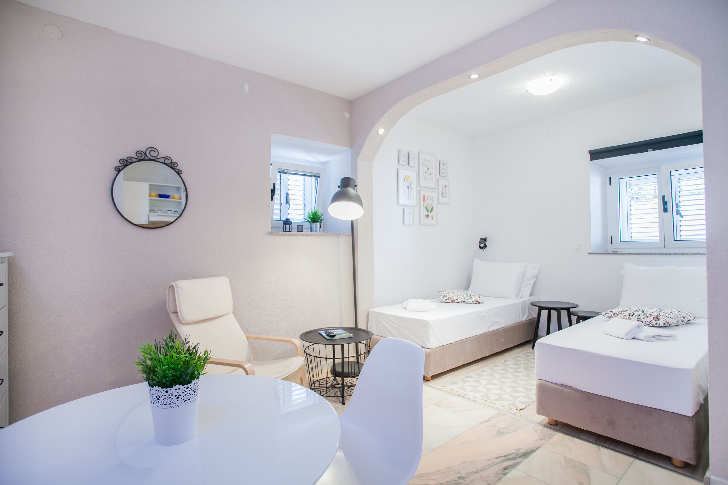 Una habitación compacta y bien iluminada, con una cama, una mesita, una silla y una planta en maceta.