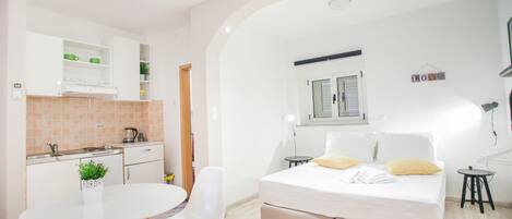 Una habitación compacta con kitchenette, una cama con dos almohadas, una mesita pequeña y una silla.