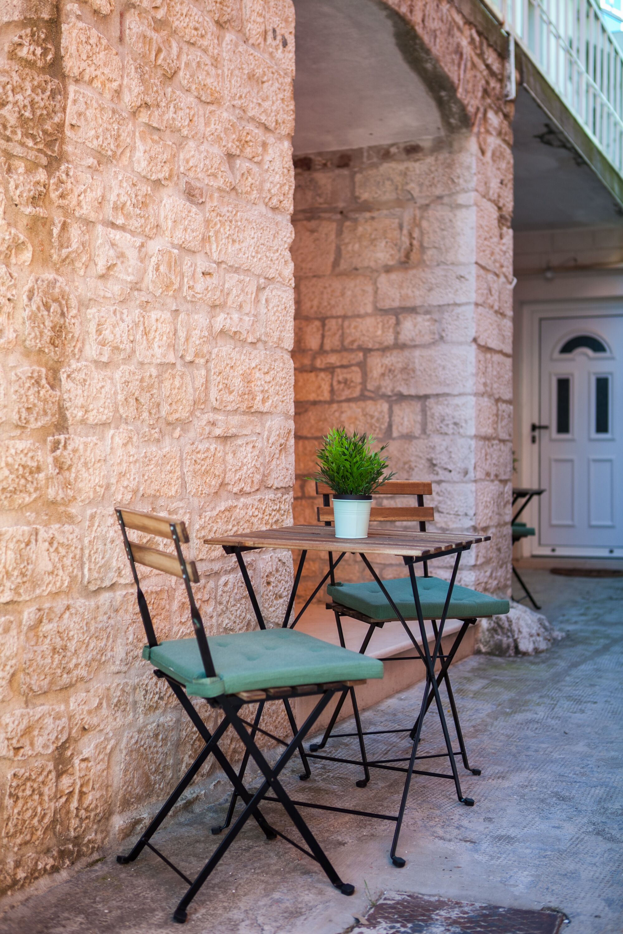 Un mur de pierre avec une table et des chaises, une plante en pot et une porte en arrière-plan.
