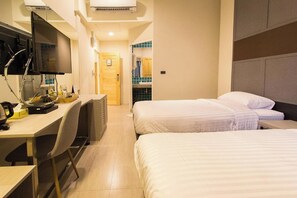 A hotel room with two beds, a desk with a computer and a chair, a TV mounted on the wall, and a bathroom visible through an open door. - Lazy Sunday Hostel (Bangkok)