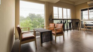 A spacious room with large windows, a seating area with chairs and a table, and a kitchen counter. - Lazy Sunday Hostel (Bangkok)