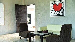 A room with two wicker chairs, a small table, and a light green sofa. A wall-mounted artwork with a red heart is visible. - Home Elements Khaoyai (Pak Chong)