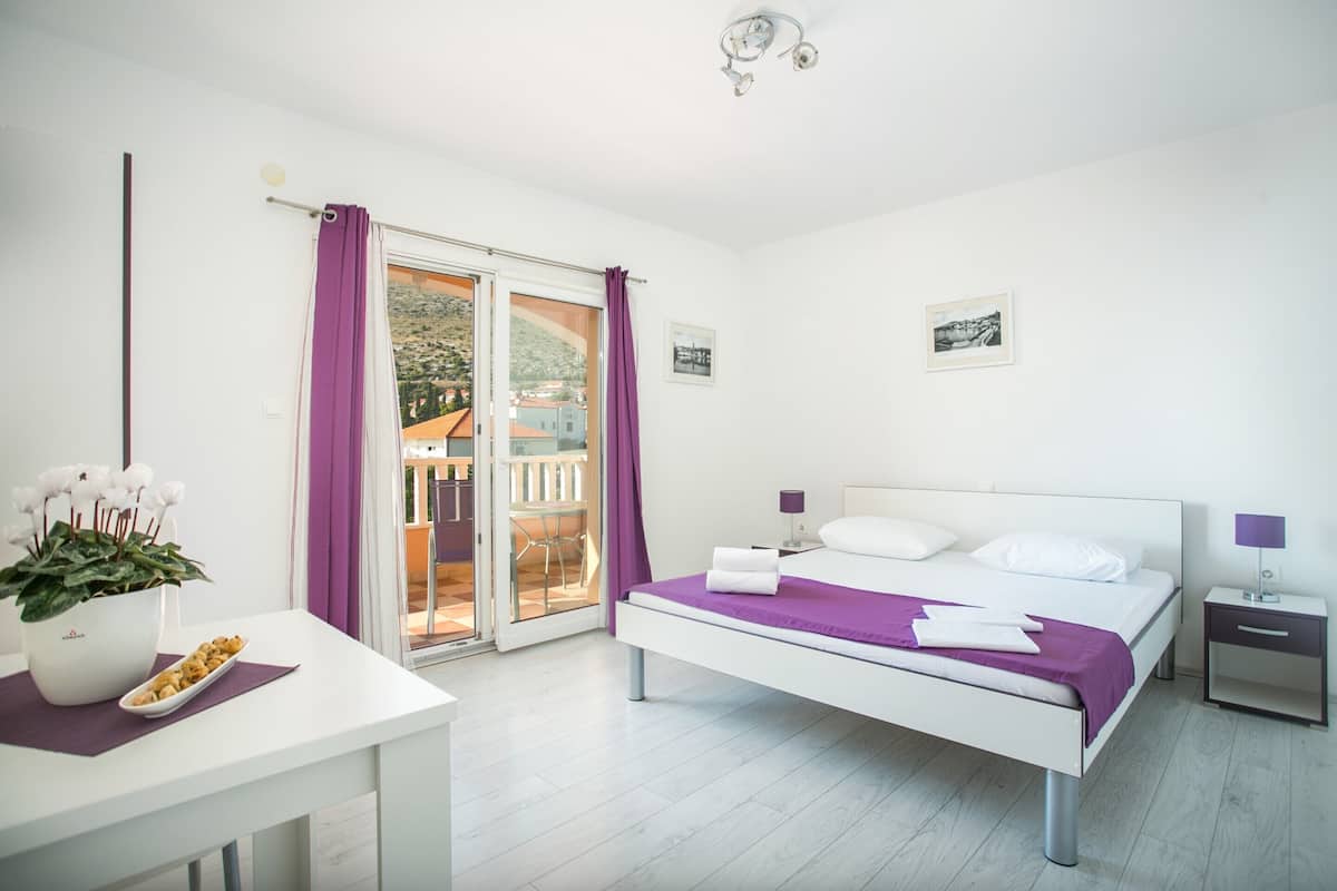 A modern bedroom with a bed, bedside tables, a desk, and a potted plant.