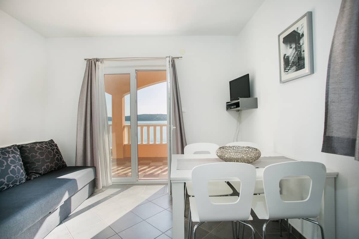 A modern room with a sofa, a dining table with chairs, a TV, and a balcony with a view.