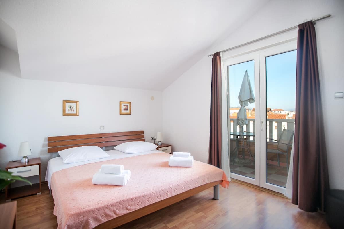 A bedroom with a bed, nightstands, a window with curtains, and a view of buildings outside.