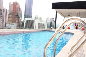 A swimming pool with a cityscape view, including high-rise buildings and a modern building with a sign.