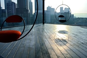 A high-rise building with a wooden deck and two circular hanging chairs.