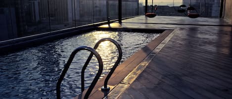 A rooftop pool with a city view, metal railings, and hanging chairs.