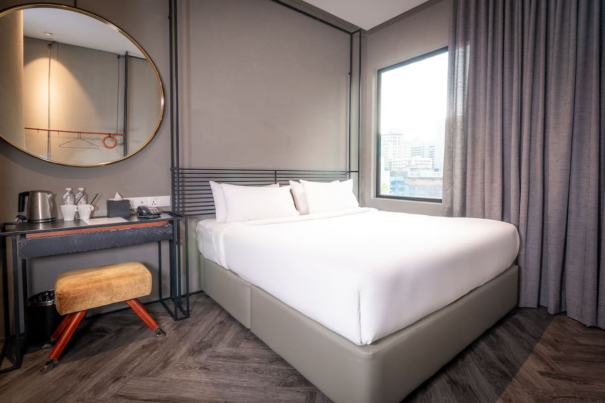 Een moderne hotelkamer met een groot bed, een bureau met stoel, een spiegel en een raam met gordijnen.