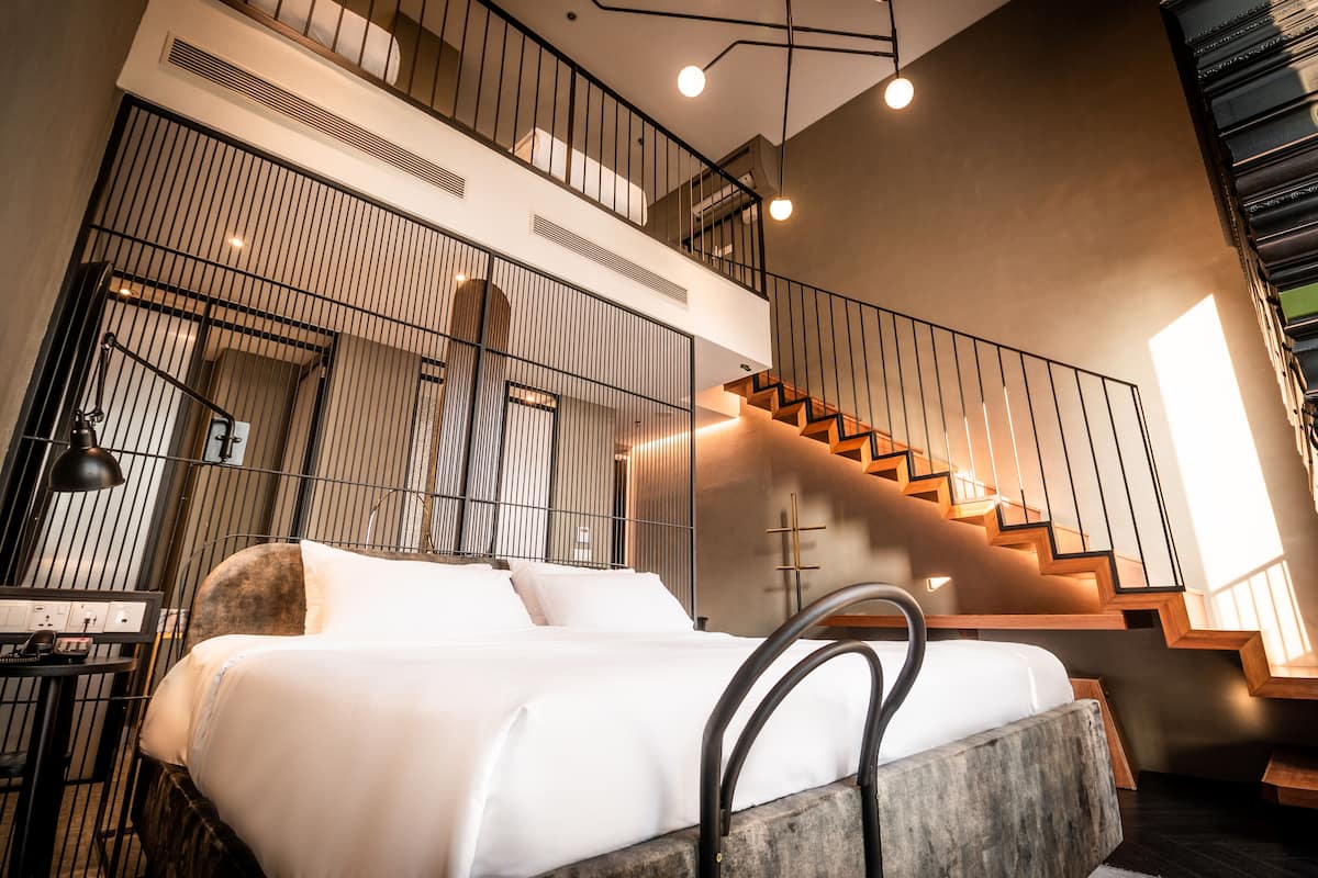 Een moderne hotelkamer met een bed, een bureau met een lamp, een groot raam en een trap.