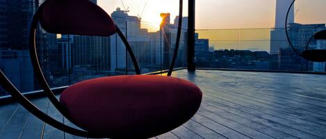 A red chair on a wooden deck with a city skyline view.