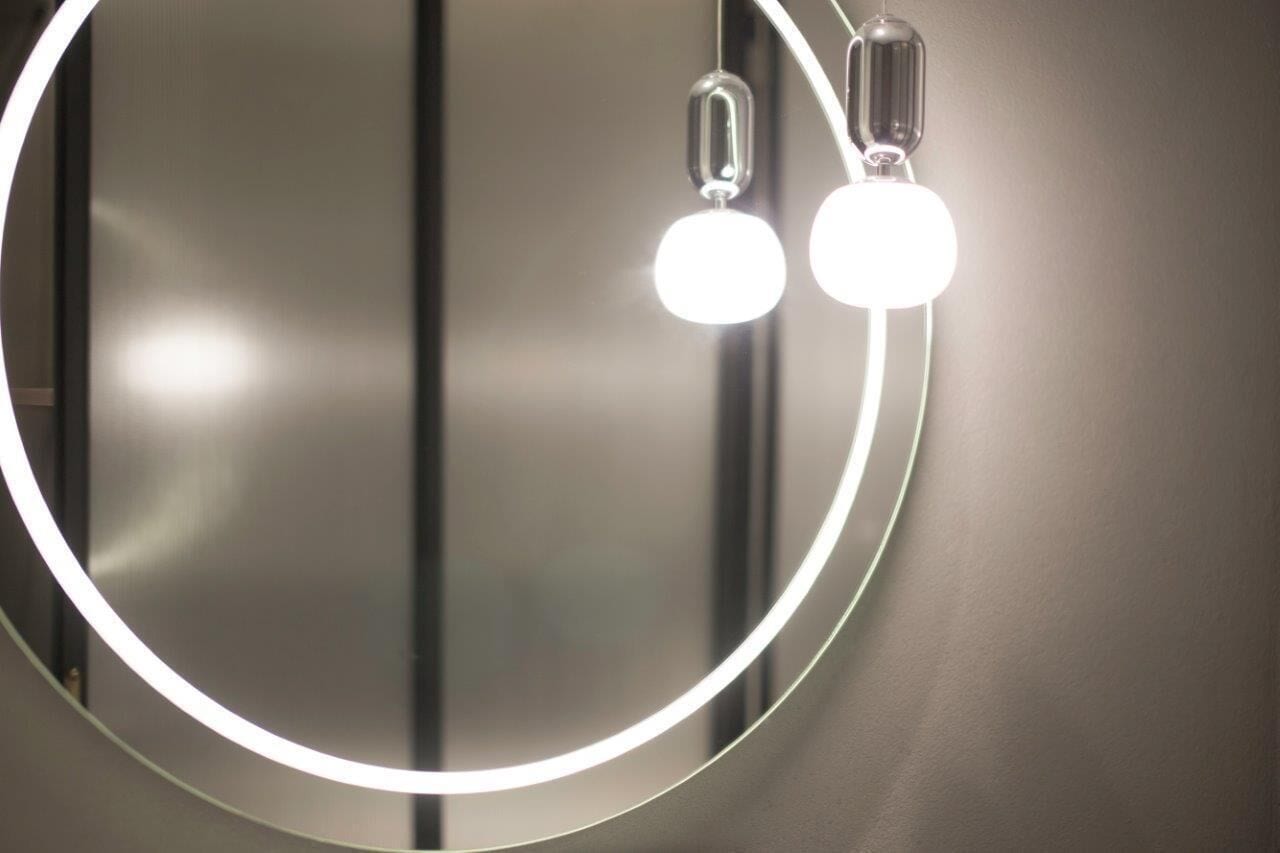 Un espejo circular con un marco iluminado y dos lámparas colgantes.