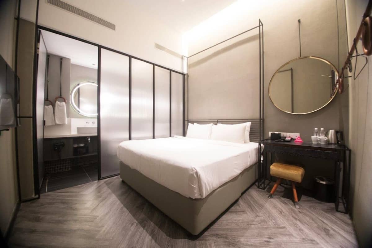 Een moderne hotelkamer met een groot bed, een kaptafel met spiegel, een klein krukje en een ronde spiegel aan de muur.