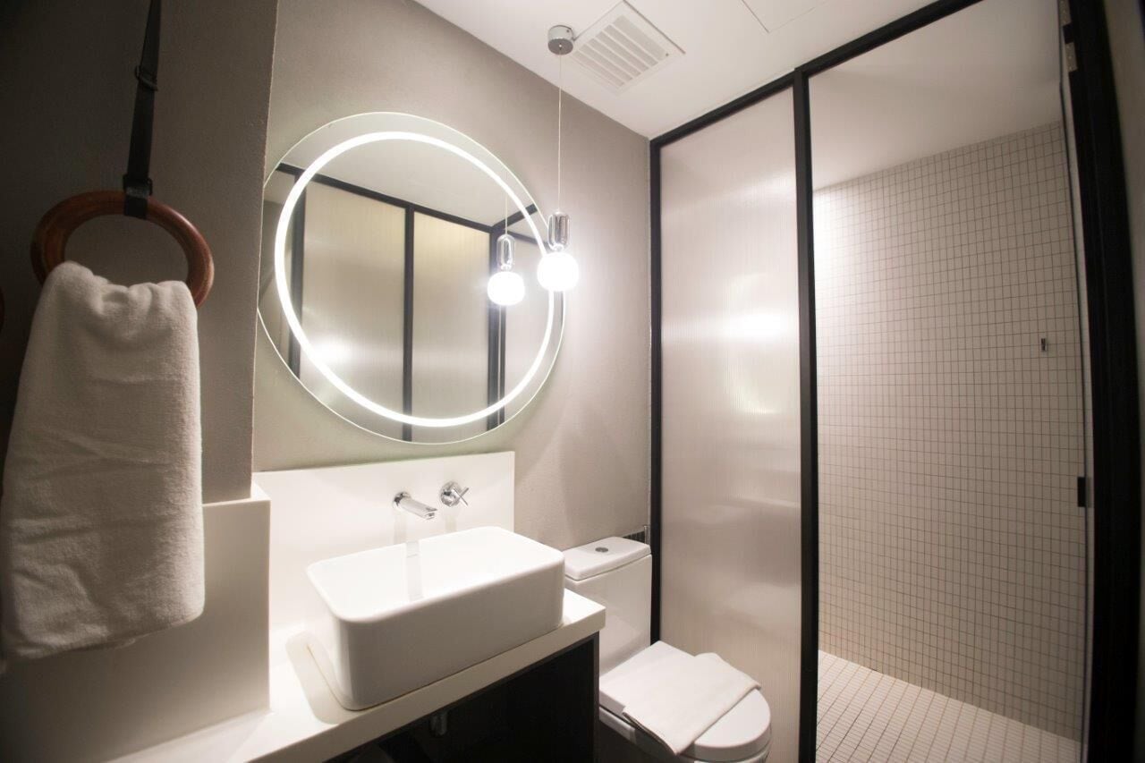 Une salle de bain moderne avec un lavabo blanc, un miroir rond avec éclairage intégré, un porte-serviettes et un espace douche.
