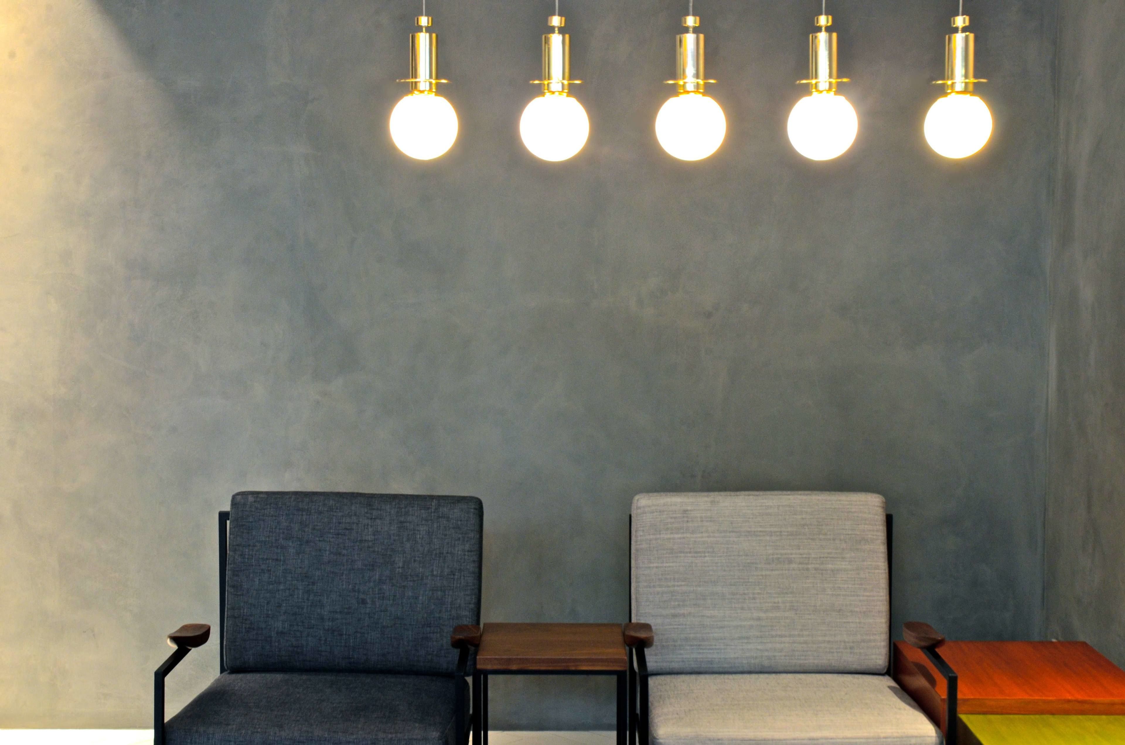 Two chairs with a small table between them, against a plain wall with five hanging light fixtures.