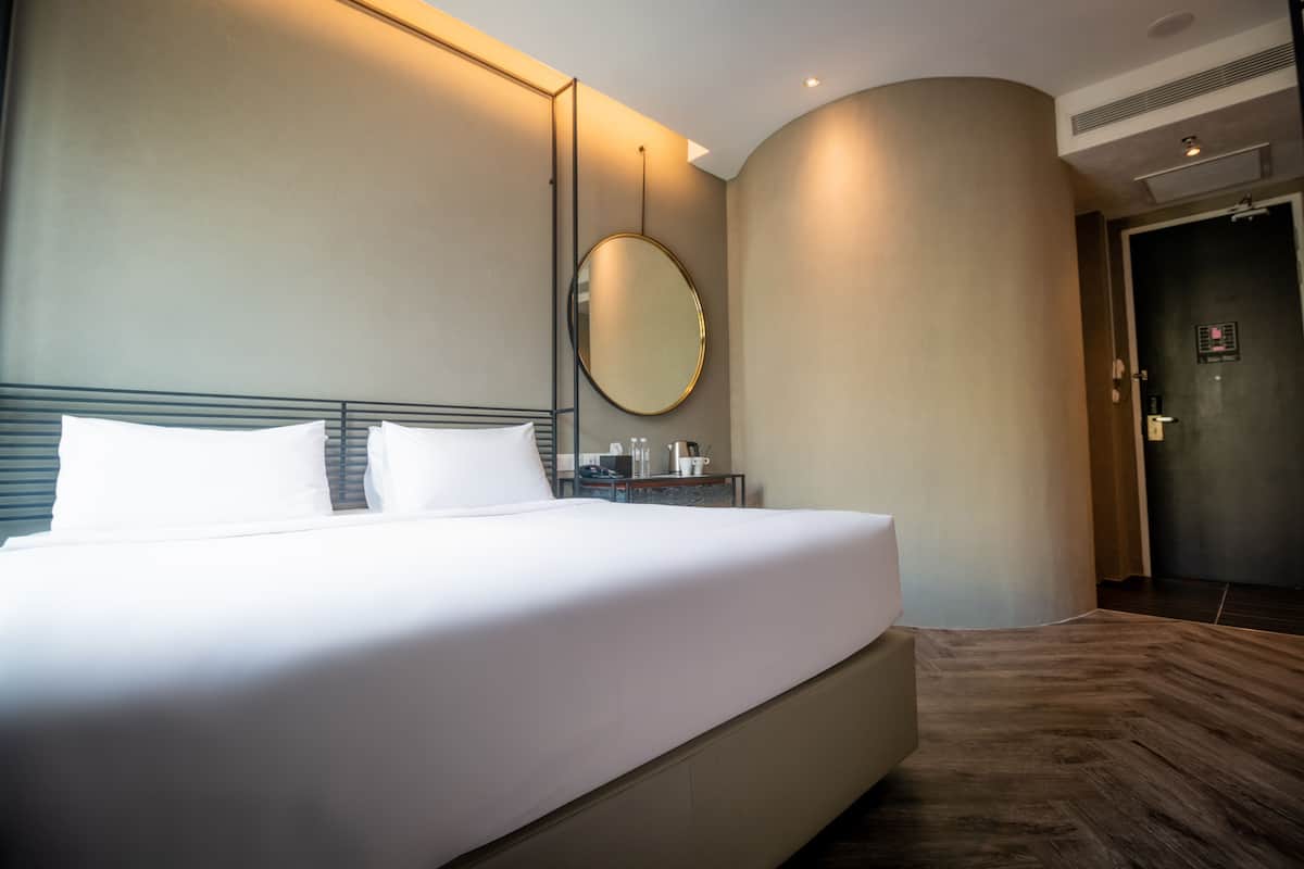 Een hotelkamer met een groot bed, een ronde spiegel, een nachtkastje en een deur.