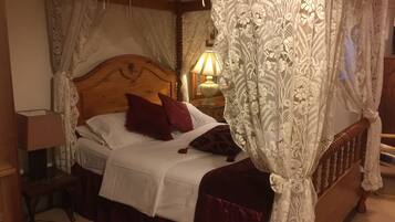 A bedroom with a wooden bed, white bedding, a red pillow, lace curtains, and a bedside lamp.