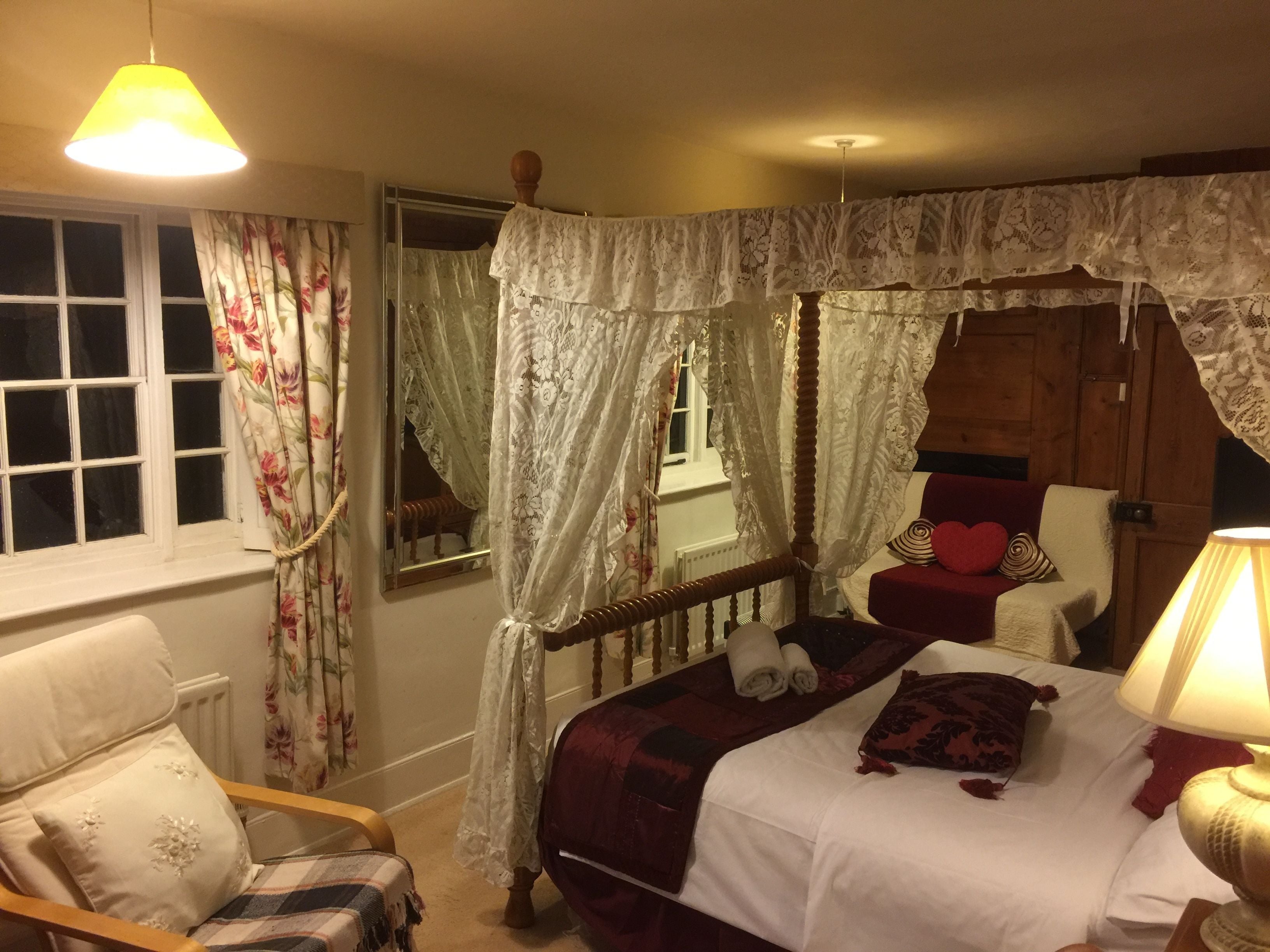 Un dormitorio con cama a dosel, una silla, una mesita de noche y una lámpara.
