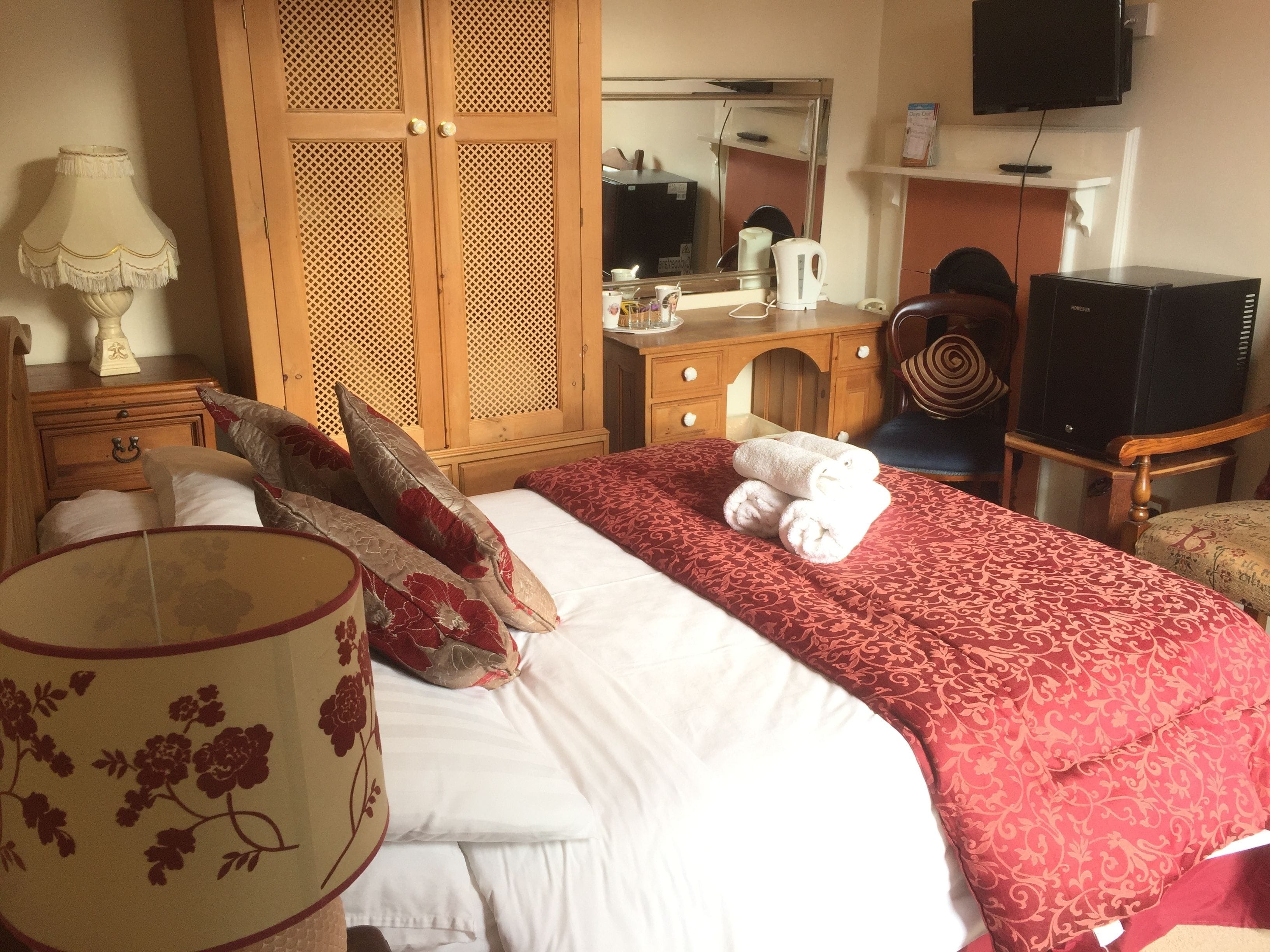 Habitación de hotel con una cama, un armario de madera, un escritorio con espejo, un televisor y una silla.