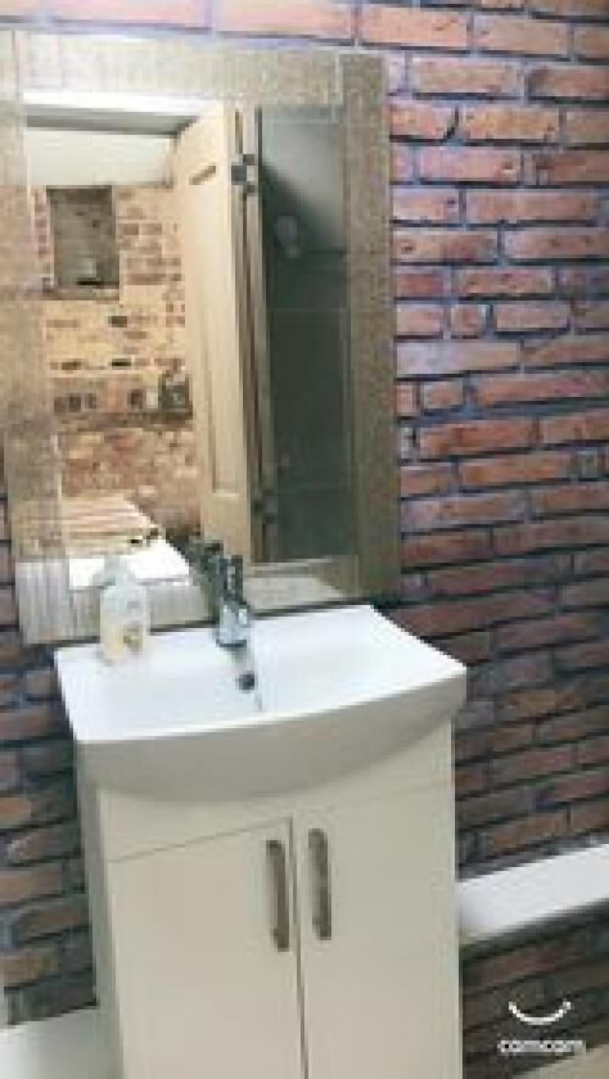 A bathroom with a white sink, a mirror, and a brick wall.