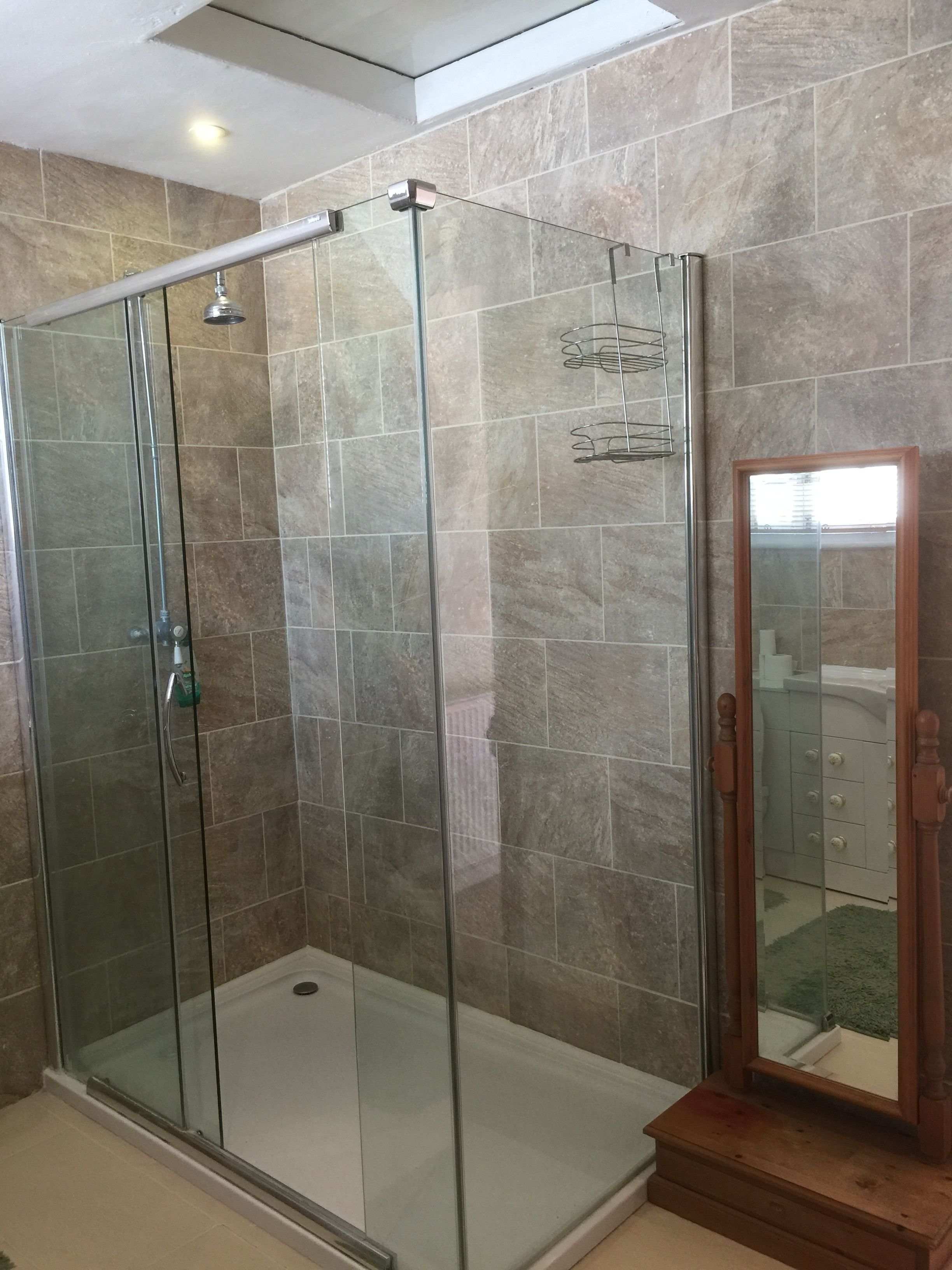 A glass-enclosed shower with a wooden base and a mirror.