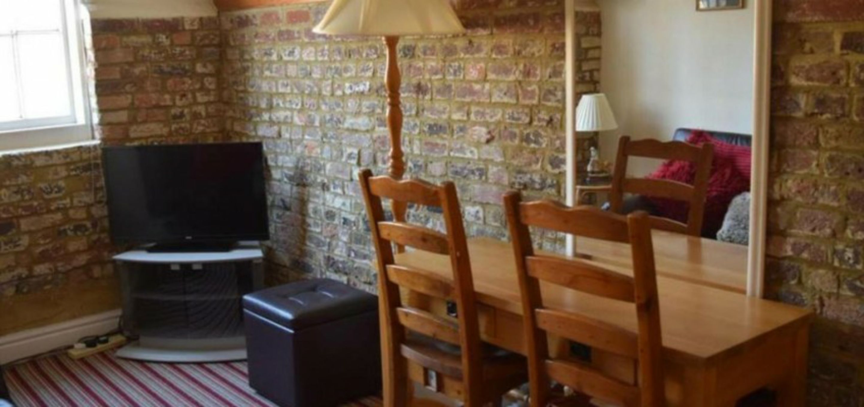 A room with a brick wall, a wooden dining table with chairs, a television, and a lamp.
