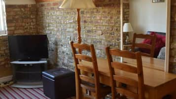 A room with a brick wall, a wooden dining table with chairs, a television, and a lamp.