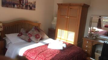 A bedroom with a bed, a wooden wardrobe, a dresser, a mirror, and a painting on the wall.